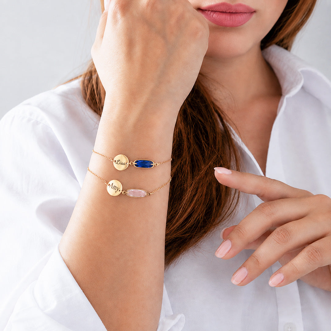Birthstone bracelets stacked on wrist showing blue and pink stones with initials
