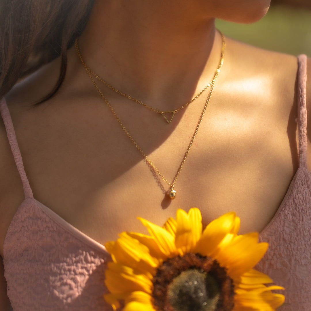 woman wearing two layered gold necklaces holding a sunflower outdoors