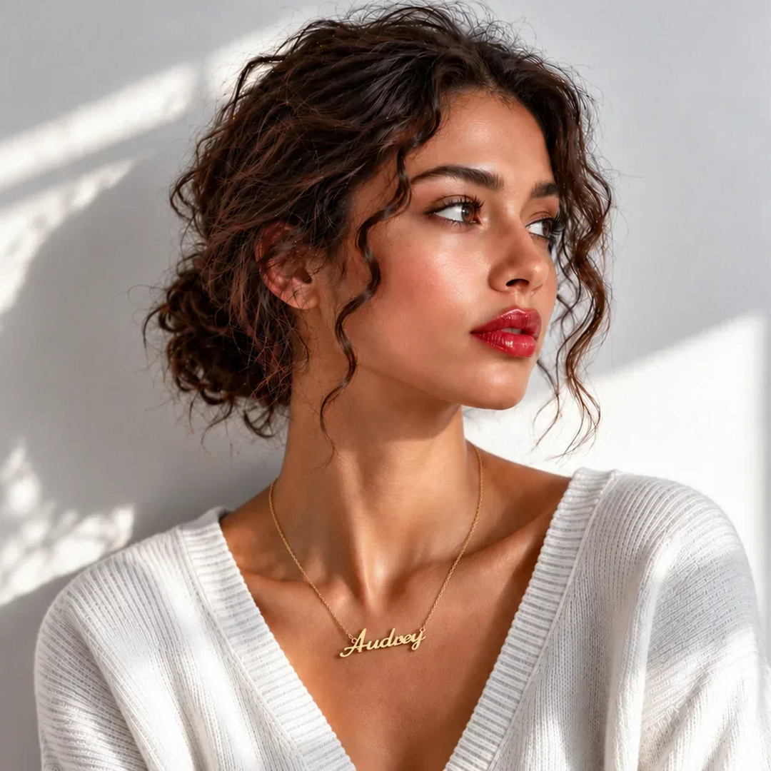 Young woman in a white sweater wearing a gold script name necklace reading Audrey
