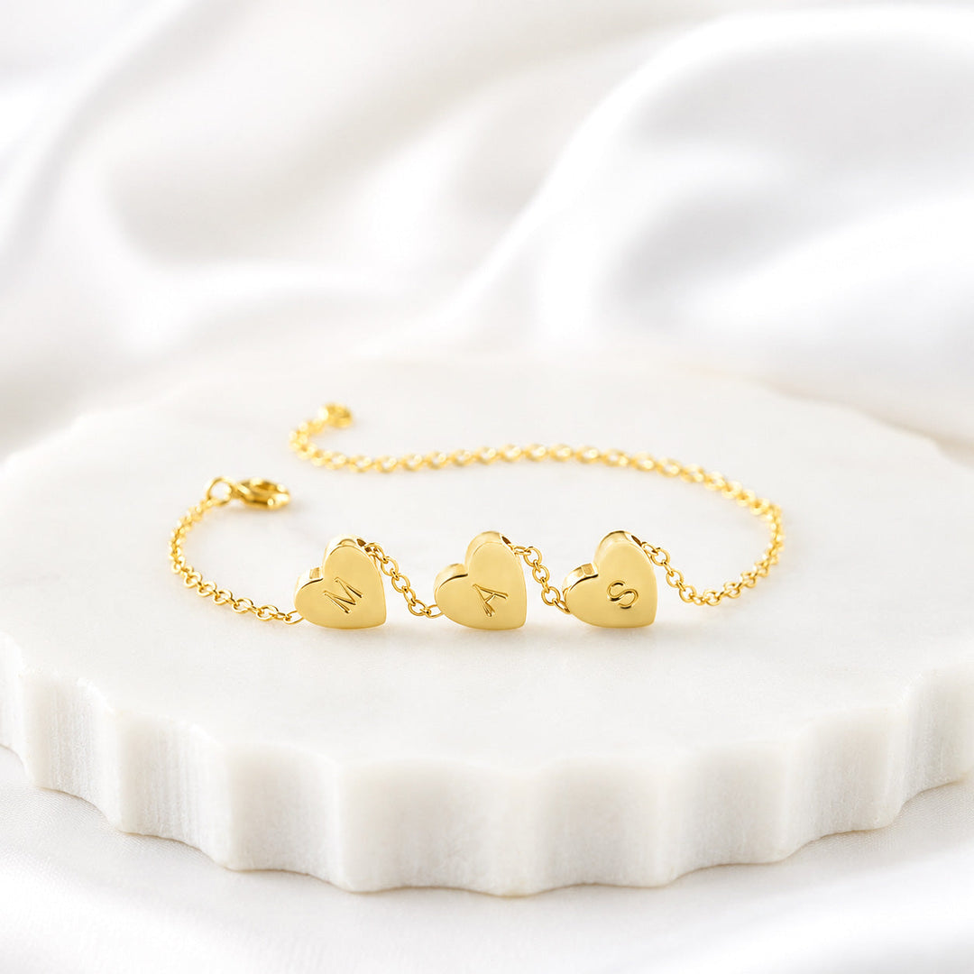 VIVO Minimalist Initial Heart Bracelet in gold vermeil displayed on white surface showing three engraved heart charms with initials M, A, and S