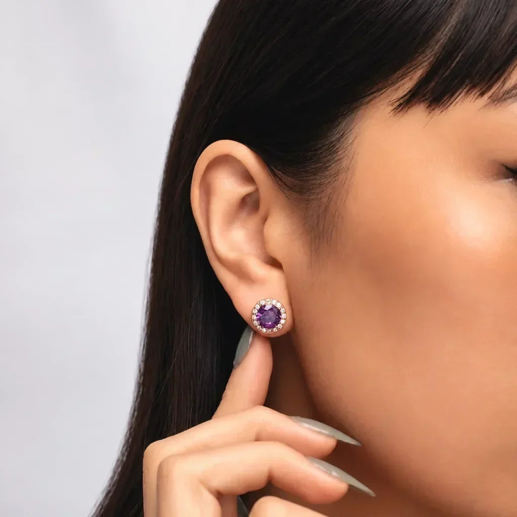 Woman wearing a 14K gold vermeil round birthstone stud earring in February amethyst color with a clear-stone halo