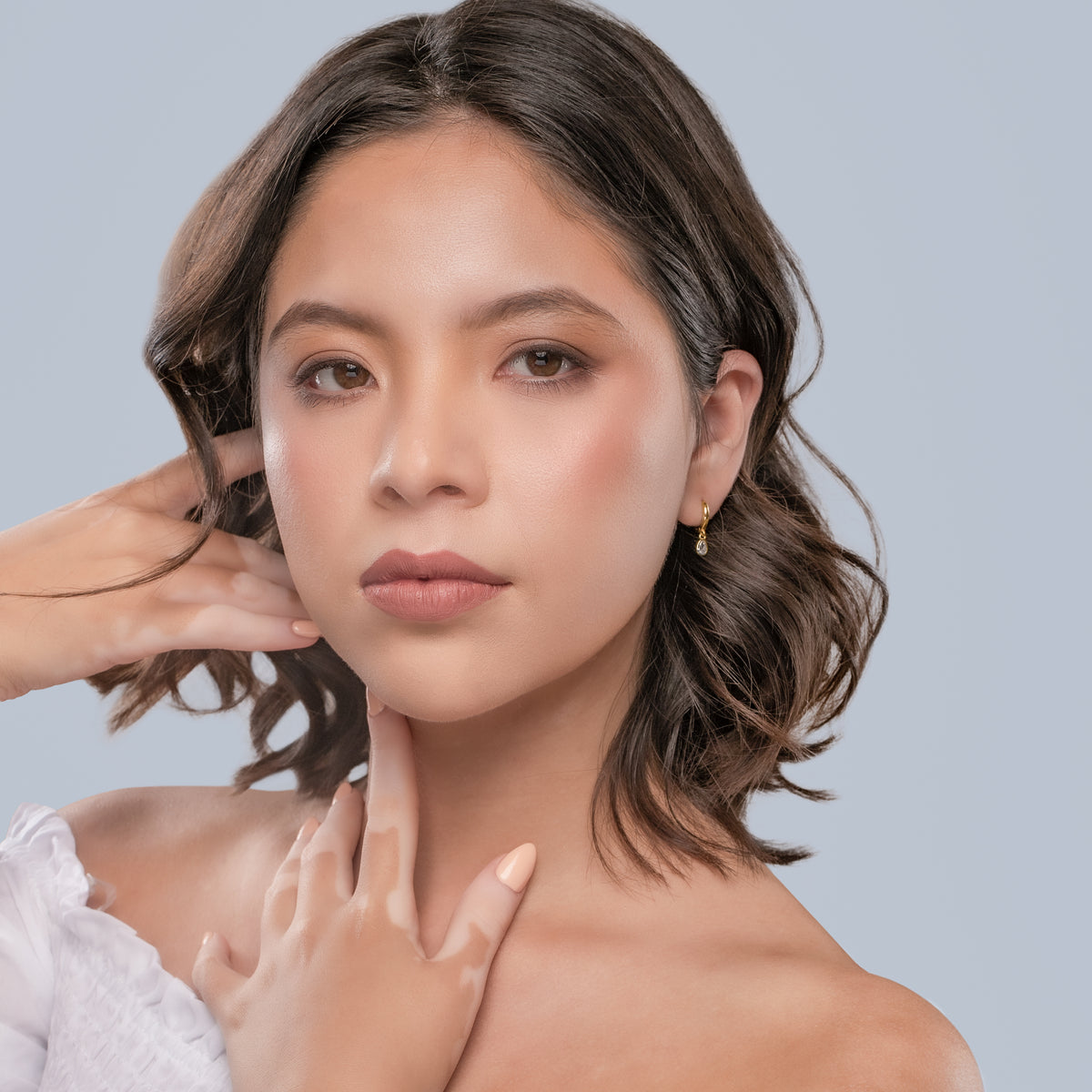 Gold-tone dangle hoop earring worn by a woman against a light gray background