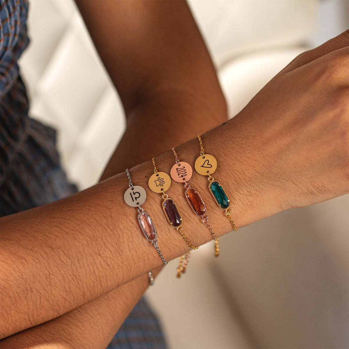 Five bracelets with engraved round discs and multicolored rectangular stones worn together on a wrist
