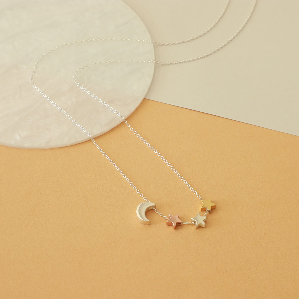 Silver-tone necklace with a crescent moon and mixed-tone star charms displayed on a beige surface