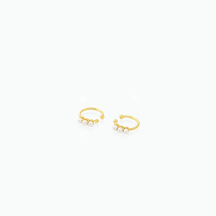 Gold ear cuffs with small pearls on a white background
