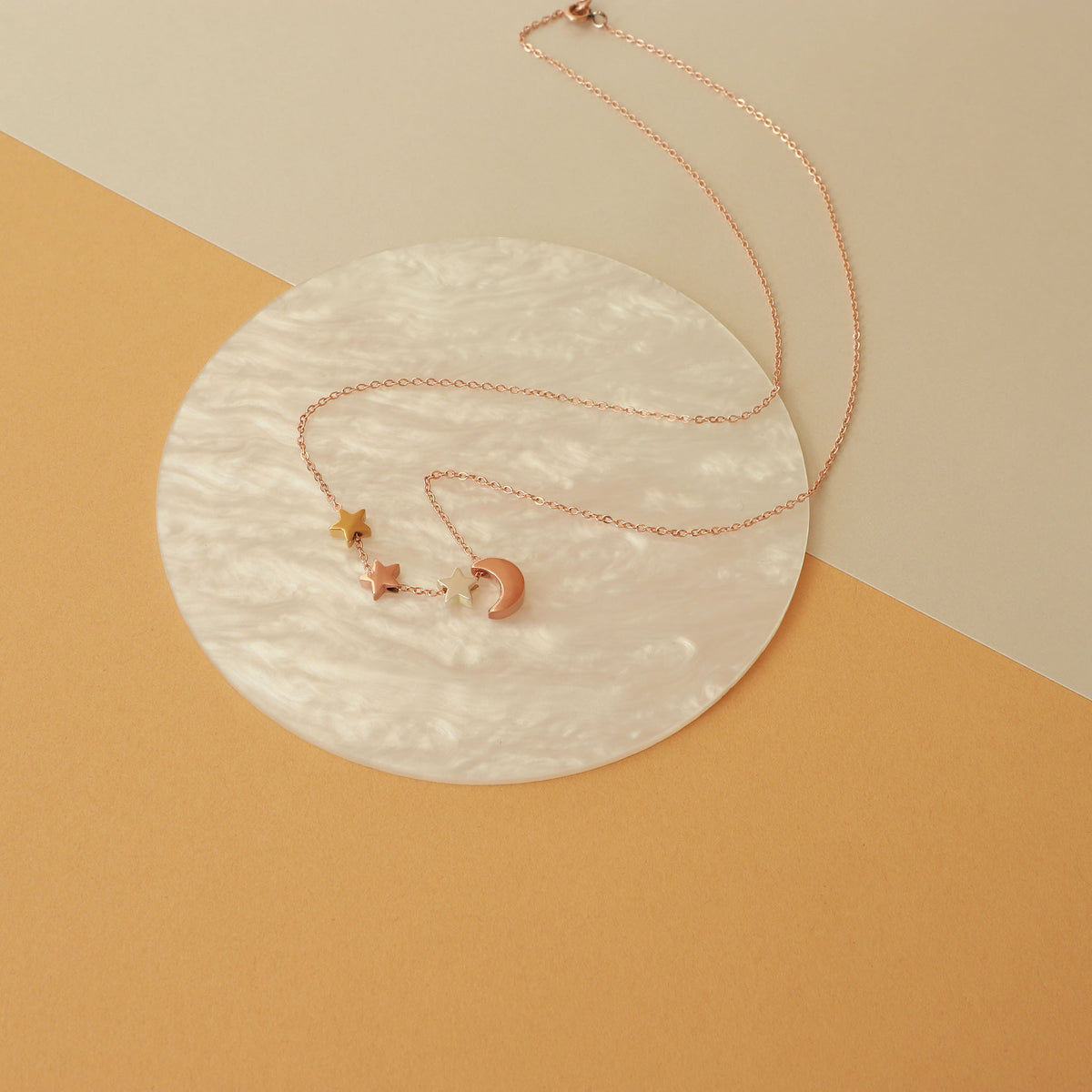 Rose-gold-tone necklace with crescent moon and star charms displayed on a round white surface