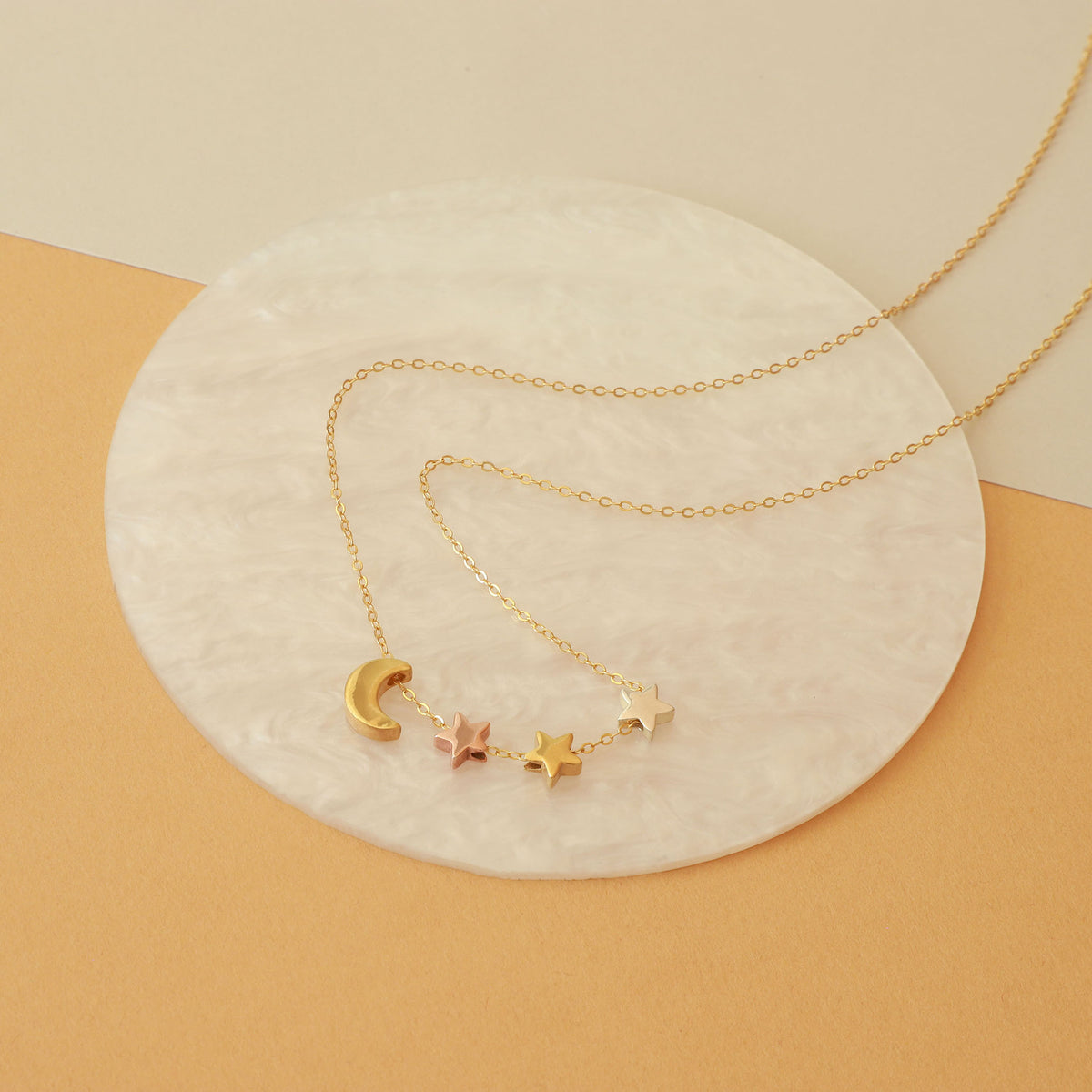 Gold-tone celestial necklace with crescent moon and star charms displayed on a round white surface