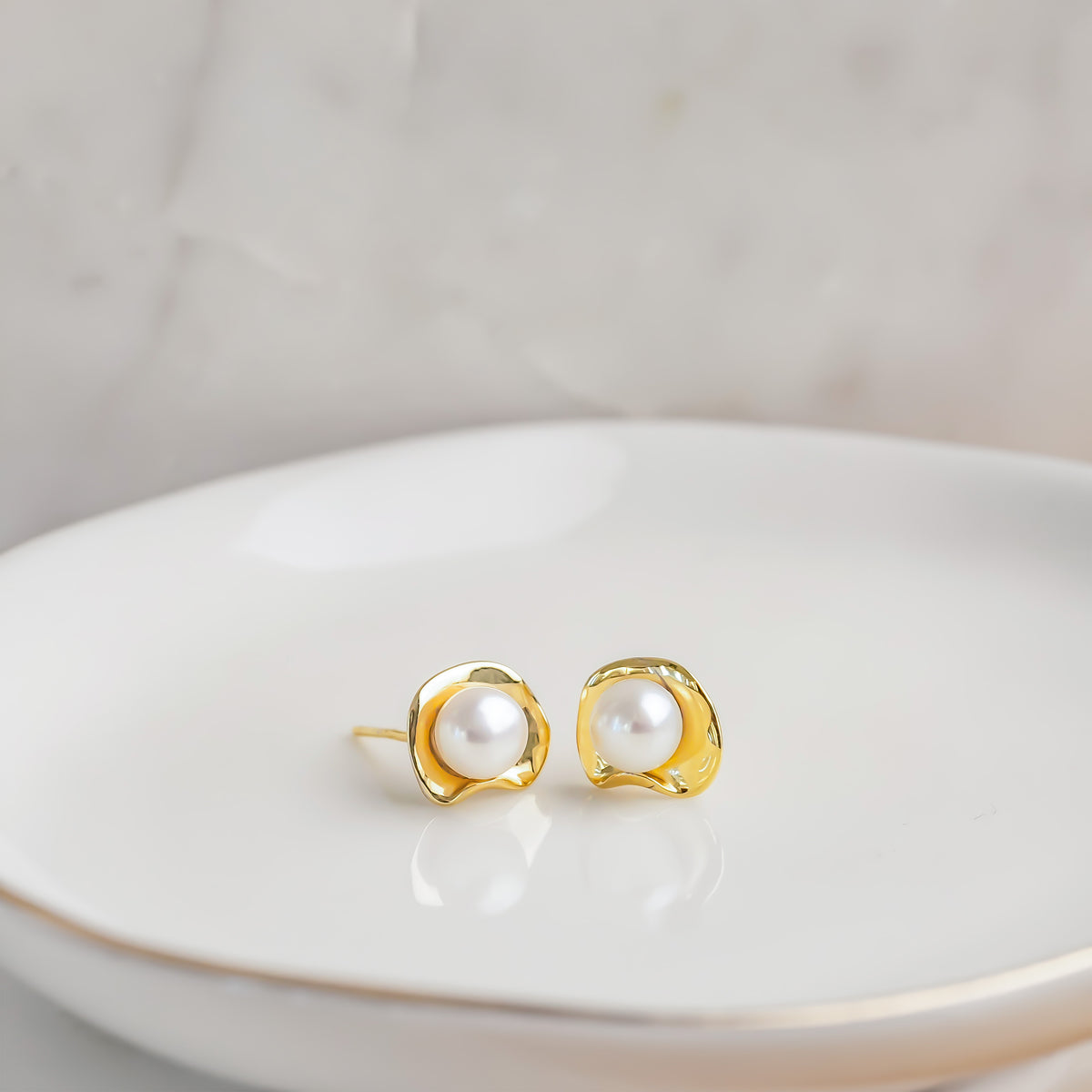 Gold-tone stud earrings with white pearl centers displayed on a white dish