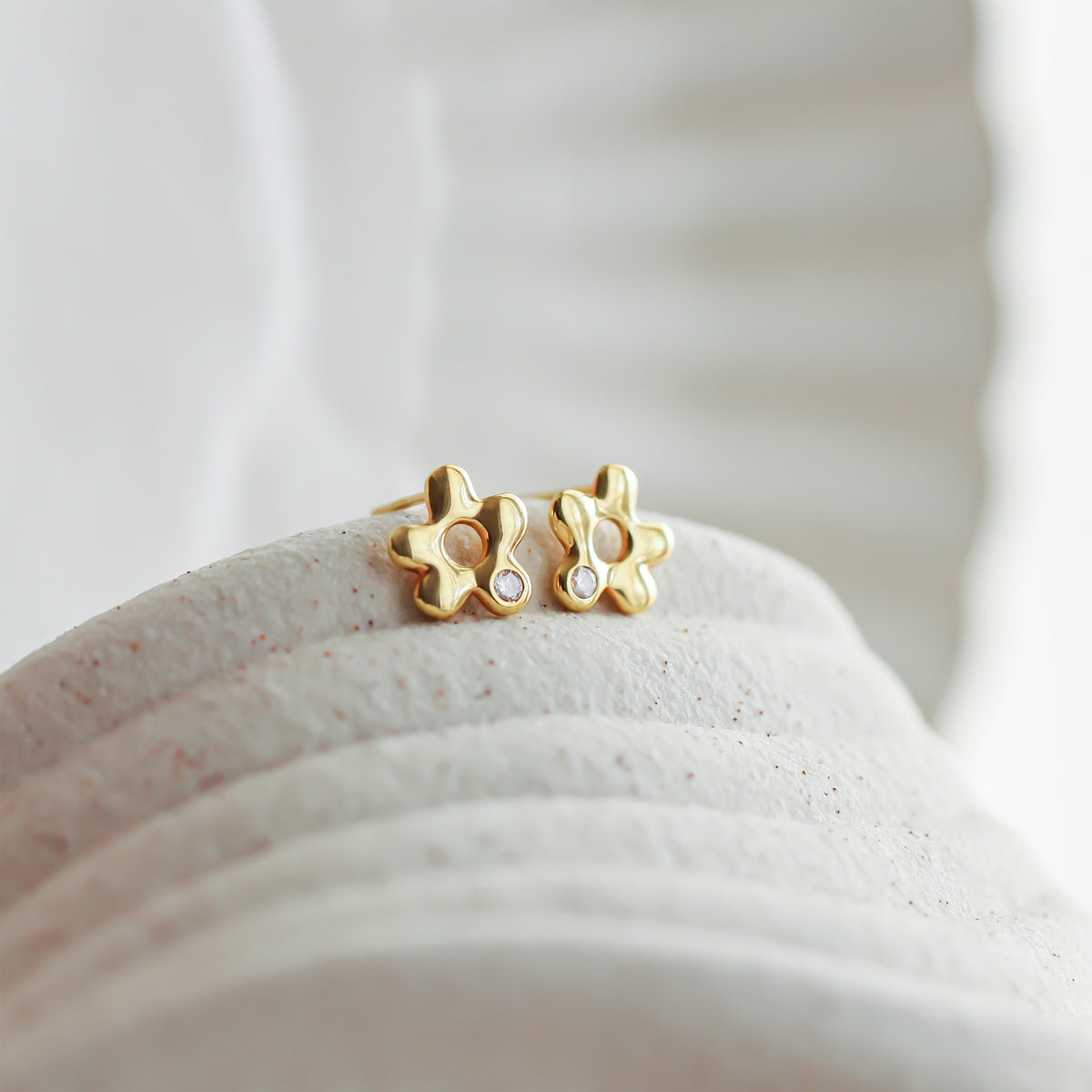 Gold-tone flower stud earrings with clear stone accents displayed on a textured white surface