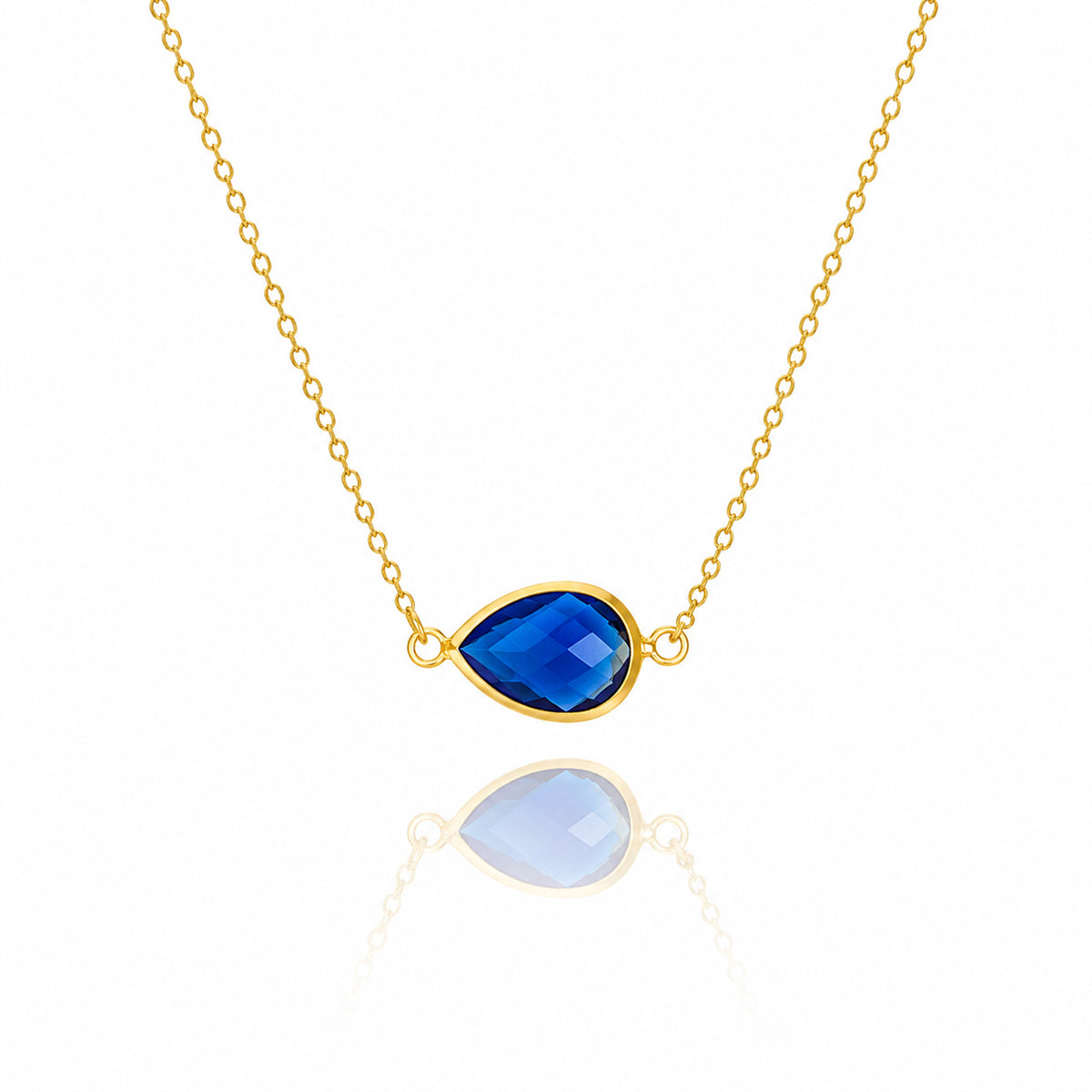 Gold-tone necklace with a dark blue faceted teardrop pendant on a white background
