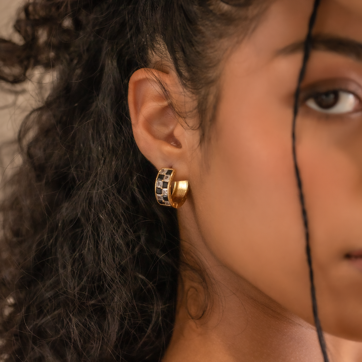 Close-up of a person wearing a gold earring with black and white stones.
