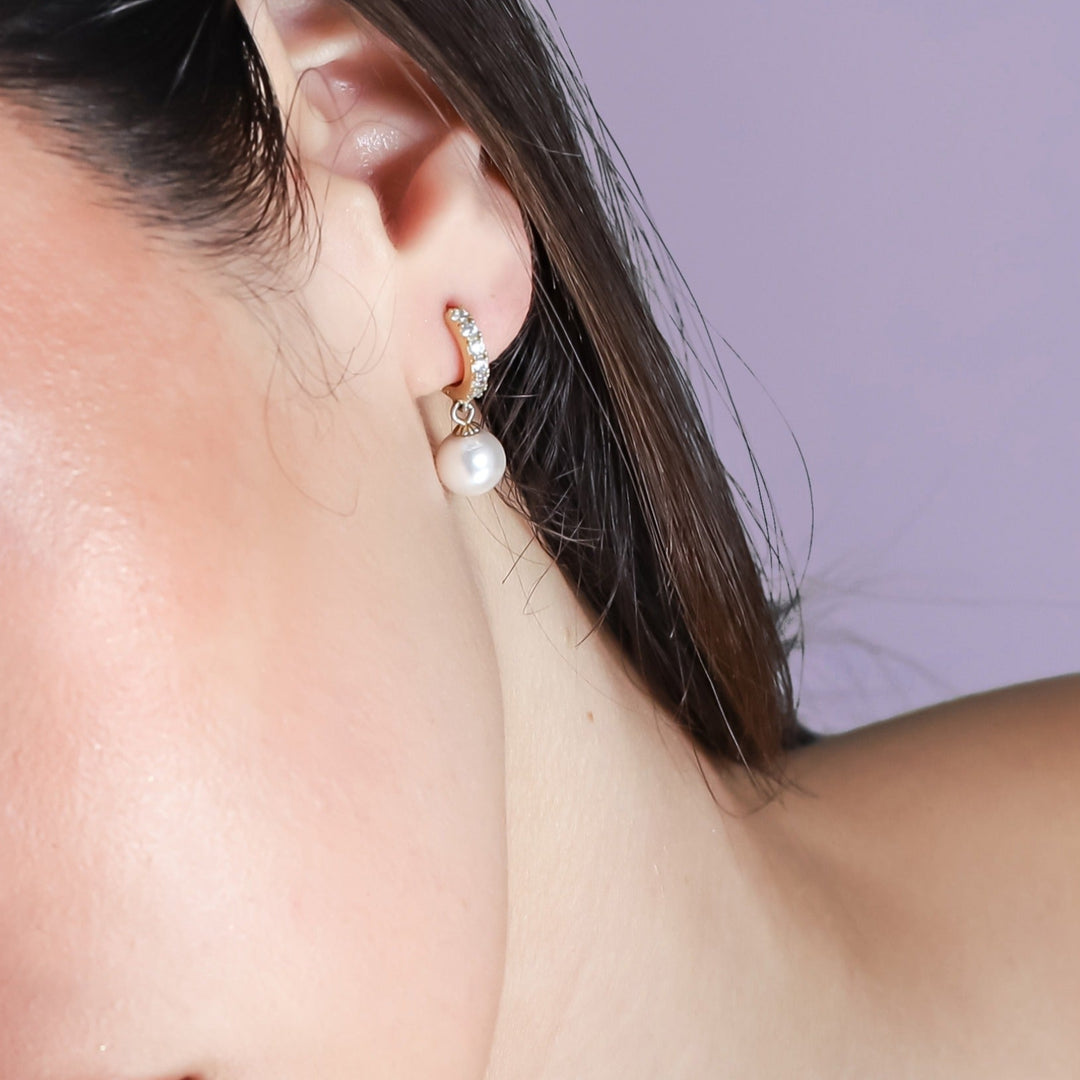 Close-up of a woman's face with a pearl earring on a light purple background