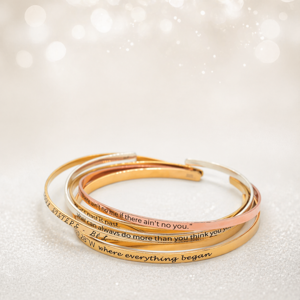Stacked gold-, silver-, and rose-gold-tone cuff bracelets with engraved messages on a light background