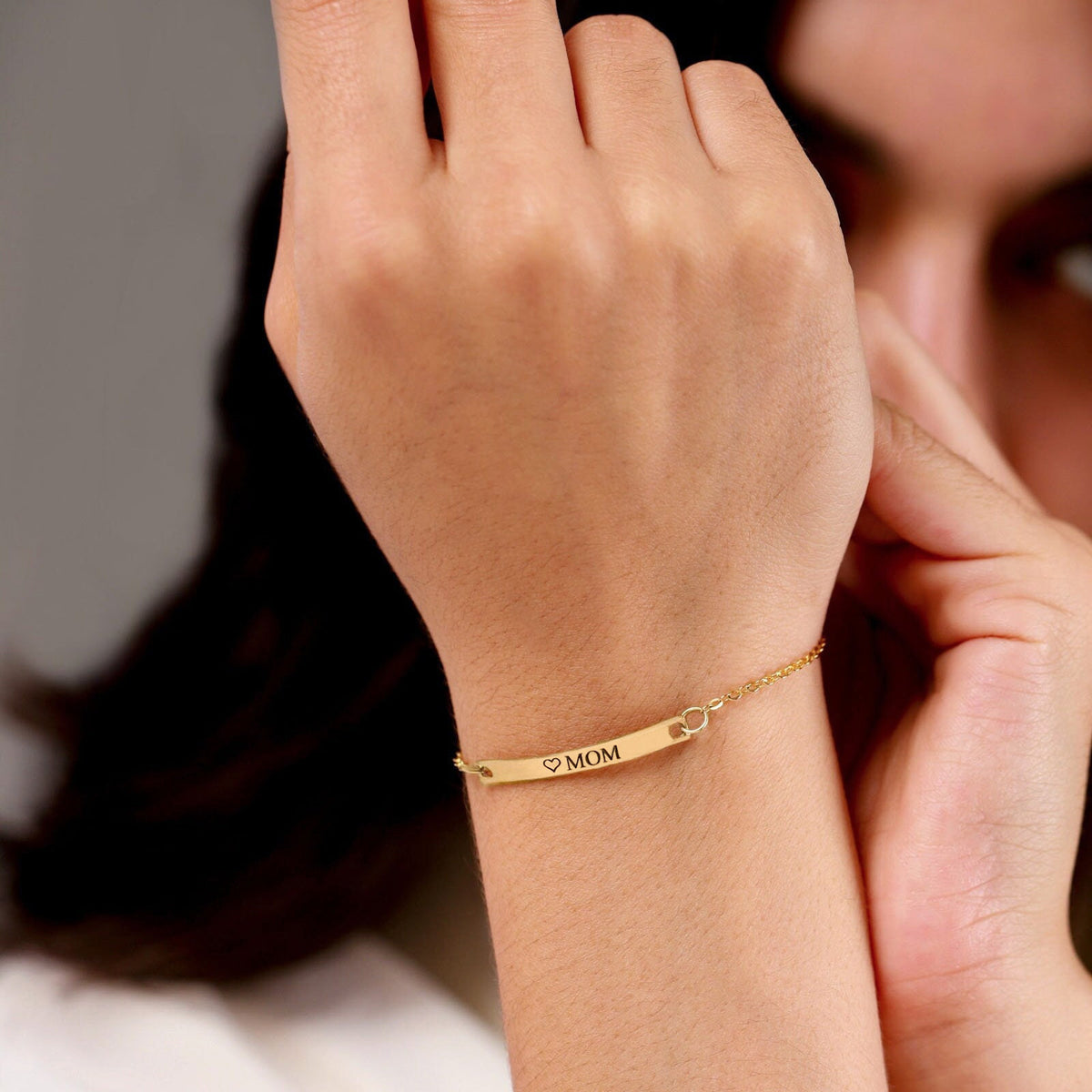 Gold-tone bar bracelet engraved with a heart and MOM worn on a wrist