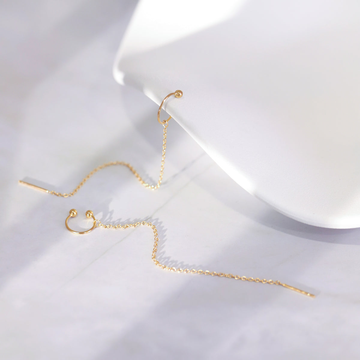 Gold chain earrings on a white surface with a white box in the background