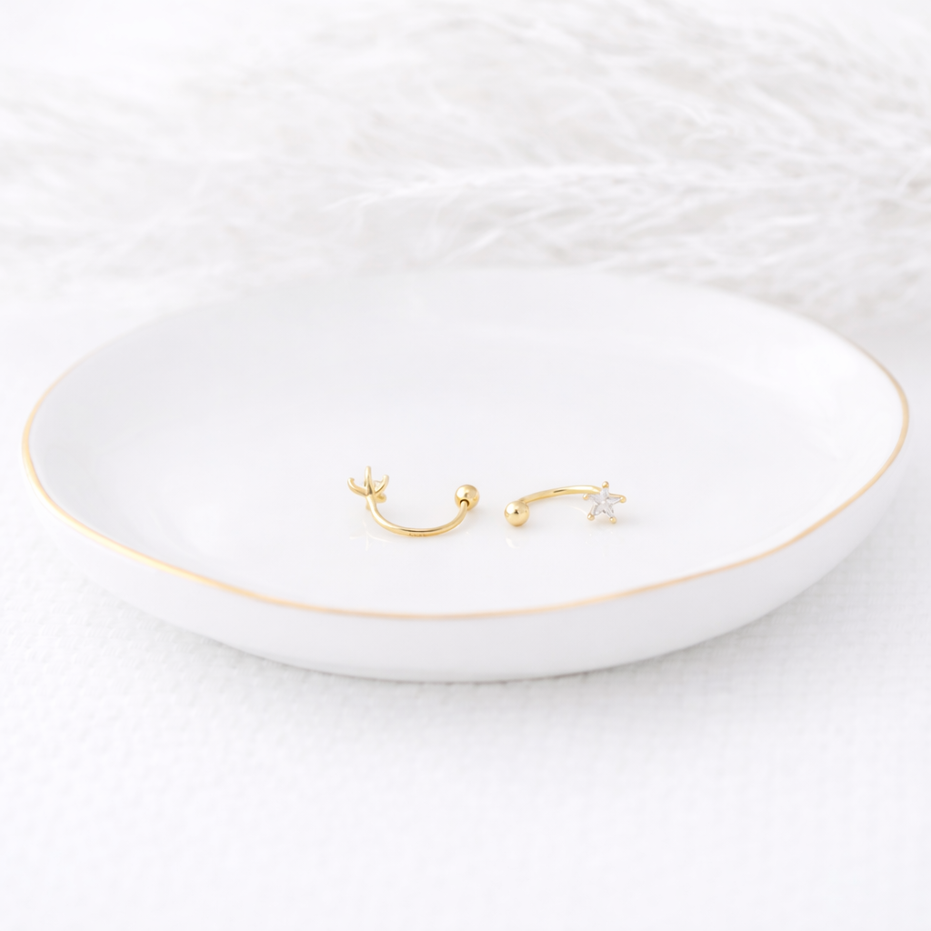 Two gold earrings on a white dish with a white background