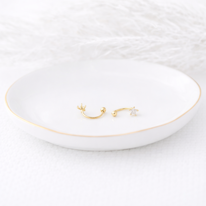 Two gold earrings on a white dish with a white background