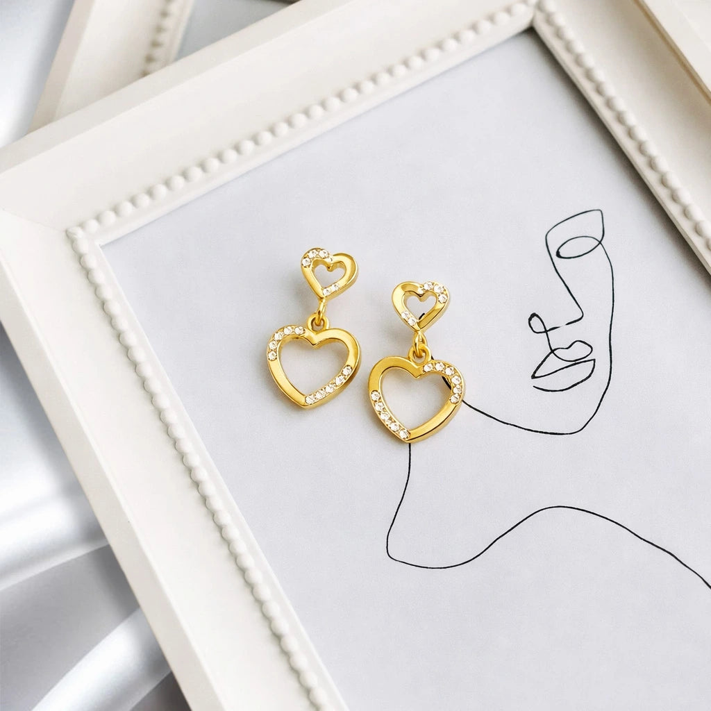 Gold heart-shaped earrings on a white surface with minimalistic design.
