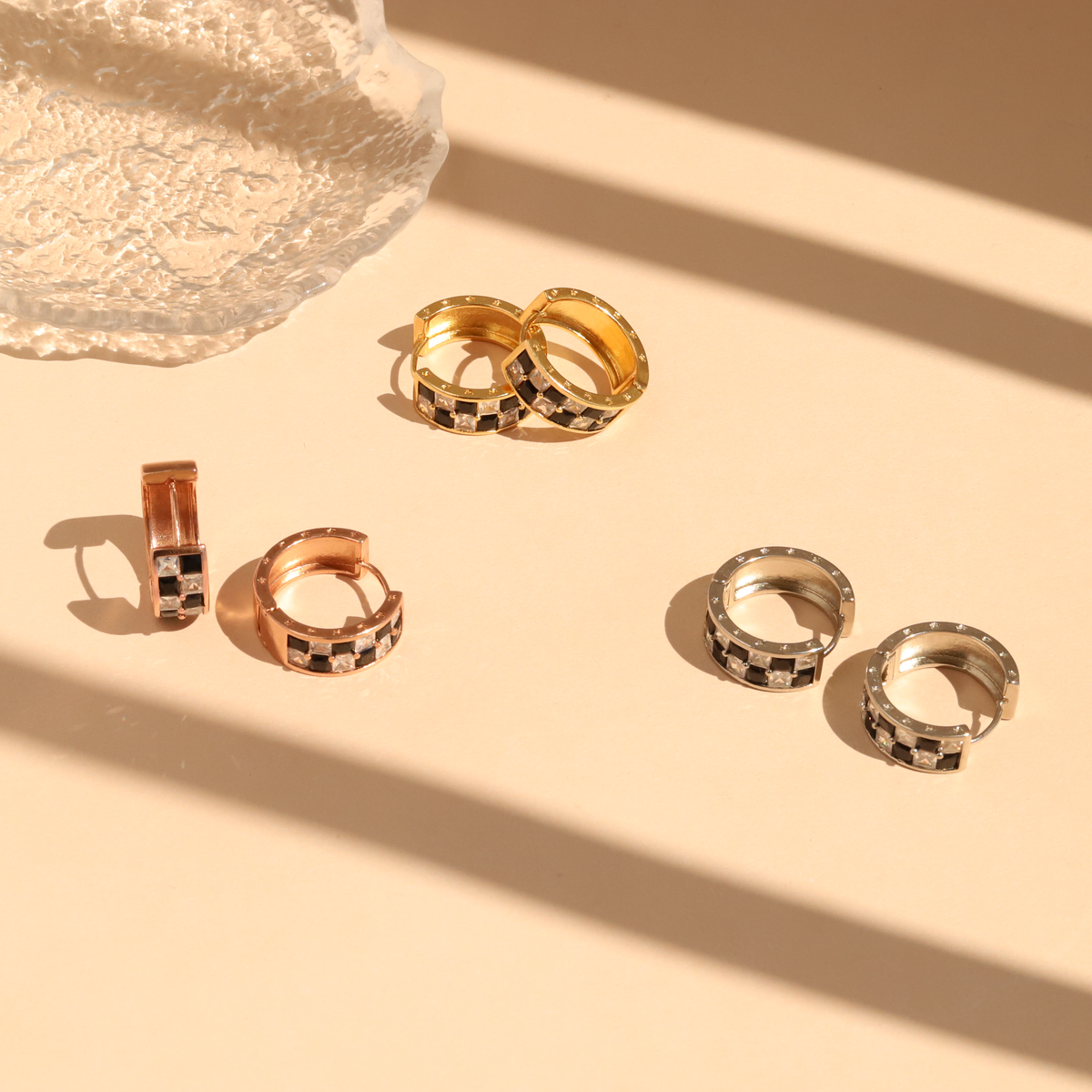 Set of gold, silver, and rose gold hoop earrings on a beige surface with a stone in the background