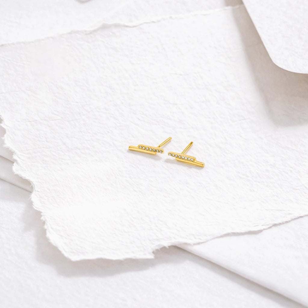 Gold bar earrings with small diamonds on a white textured surface