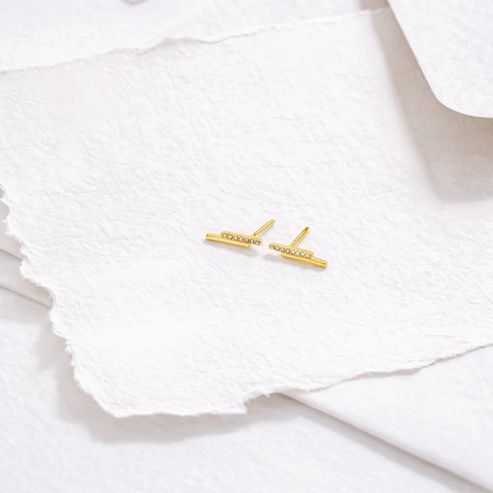 Gold bar earrings with small diamonds on a white textured surface