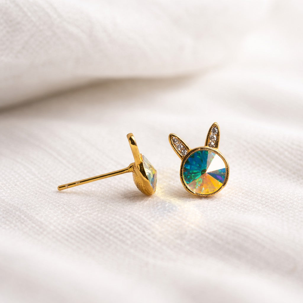 Gold earrings with colorful gemstones on a white fabric background