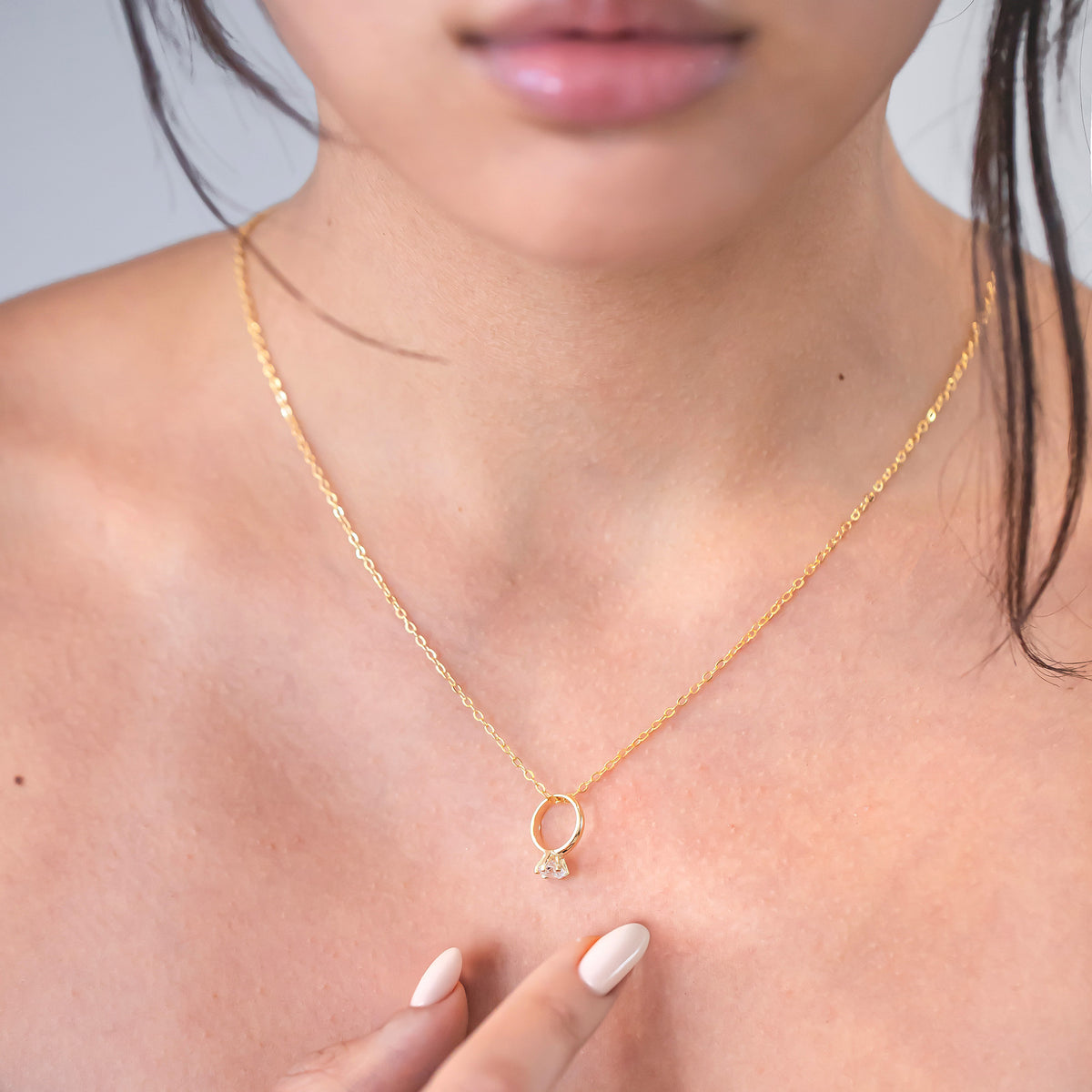 Gold-tone necklace with a ring-shaped charm and clear stone worn on a model