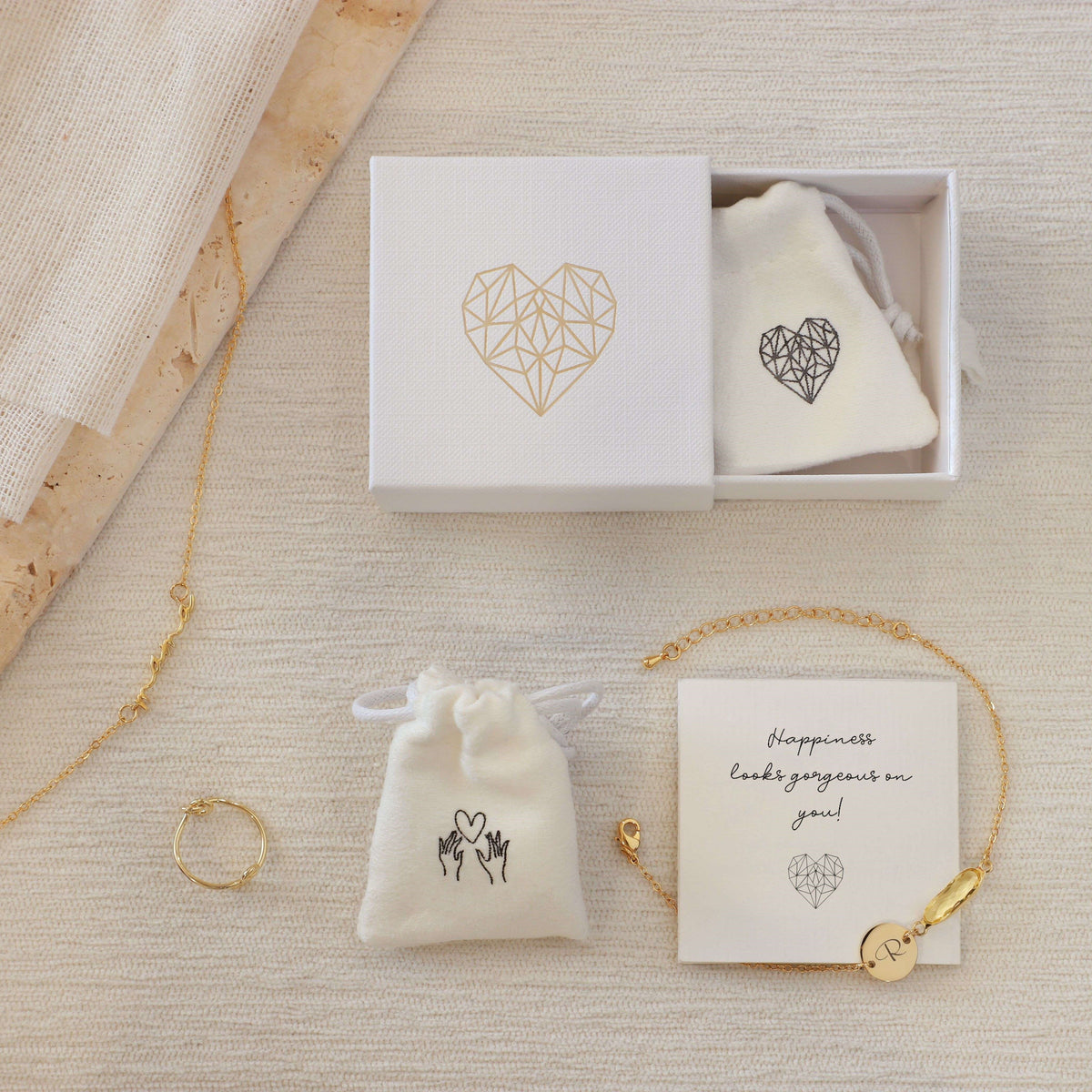 Jewelry packaging with white gift box, drawstring pouch, care card, necklace, bracelet, and ring