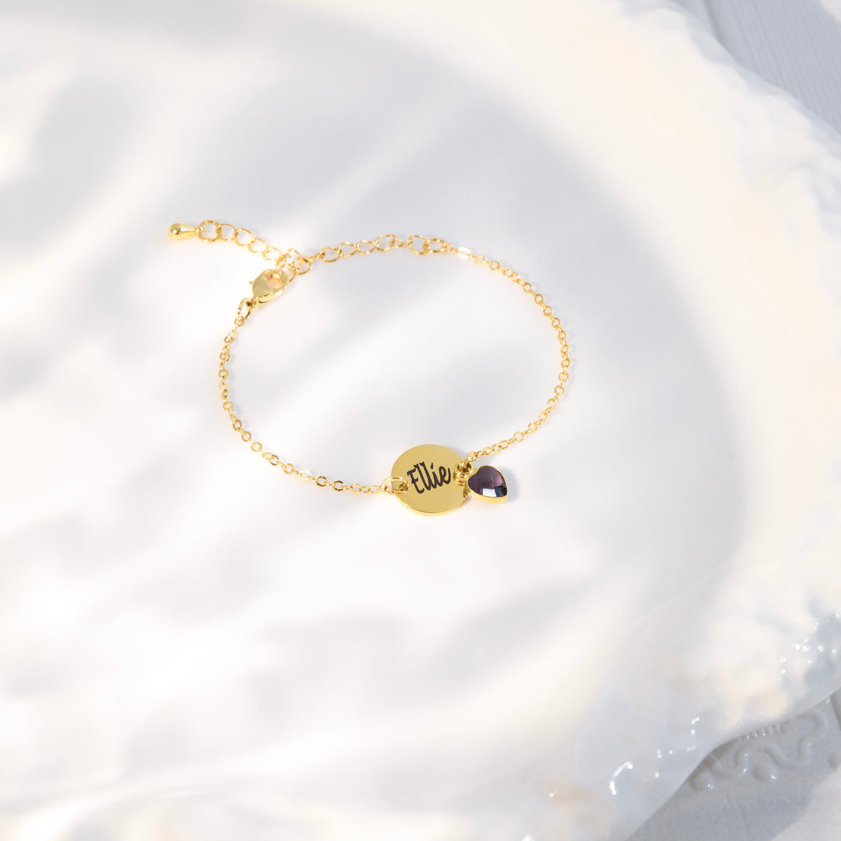 Bracelet with engraved round disc and dark faceted stone charm on white fabric