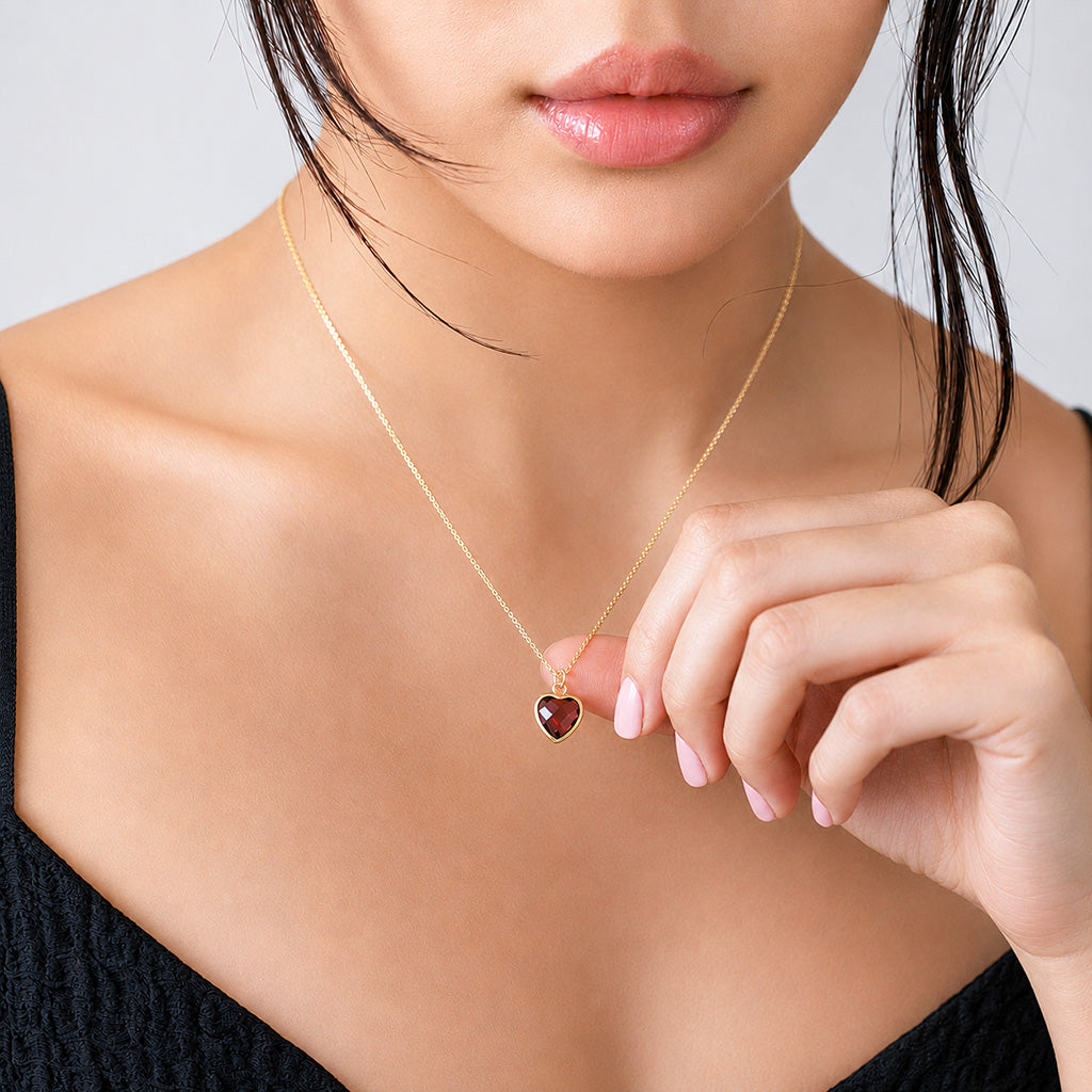 Gold-tone necklace with a red heart-shaped stone pendant worn on a model in a black top