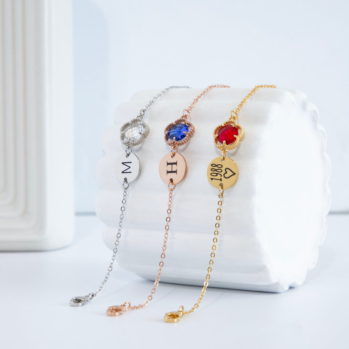 Three bracelets with M, H, and 1988 heart engravings and clear, blue, and red round stones in beaded frames