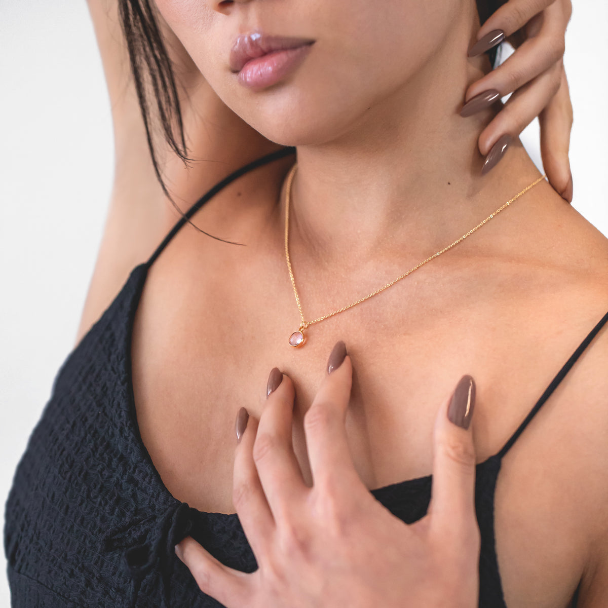 Gold-tone necklace with a round pink stone pendant worn on a model in a black top