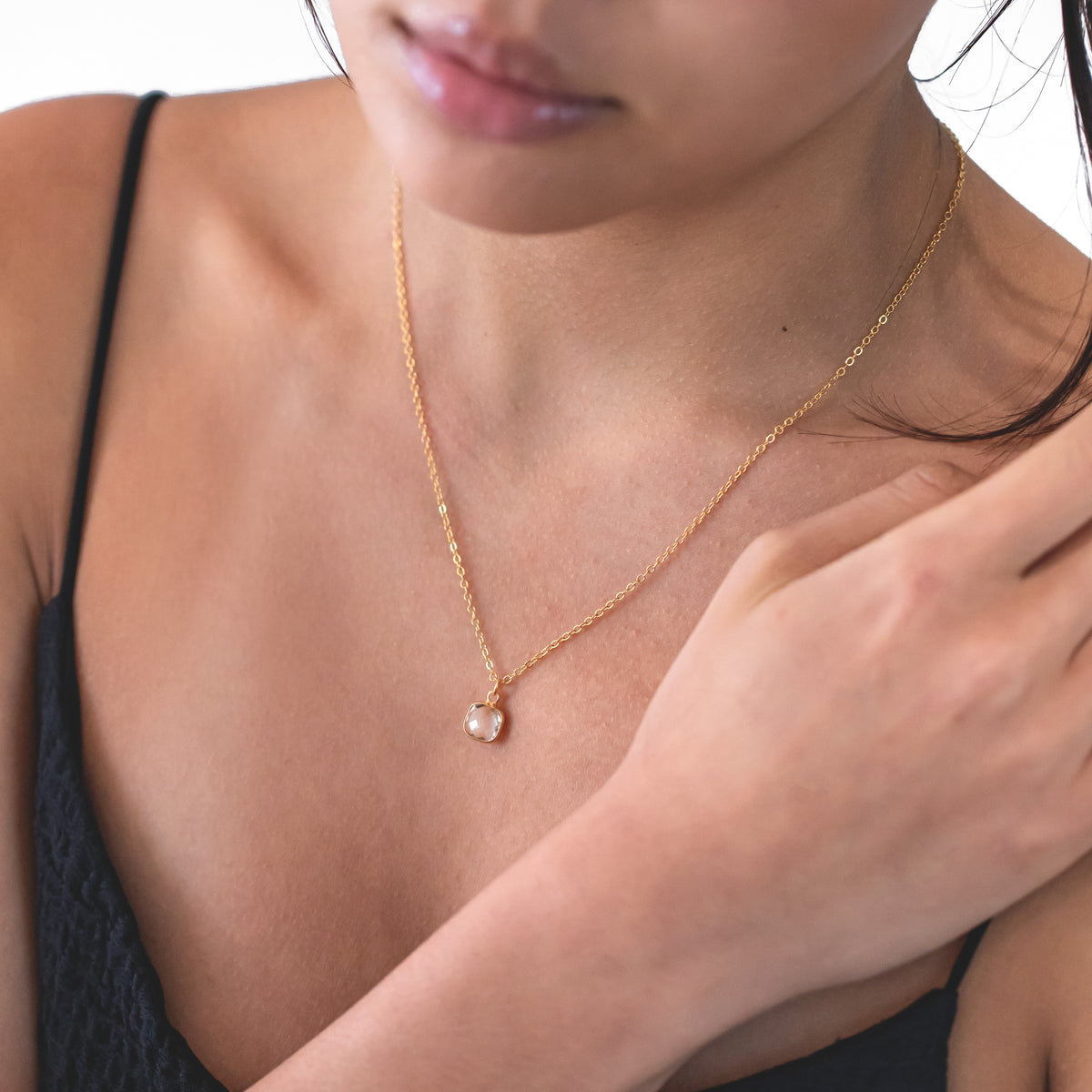 Gold-tone necklace with a small round clear pendant worn at the neckline