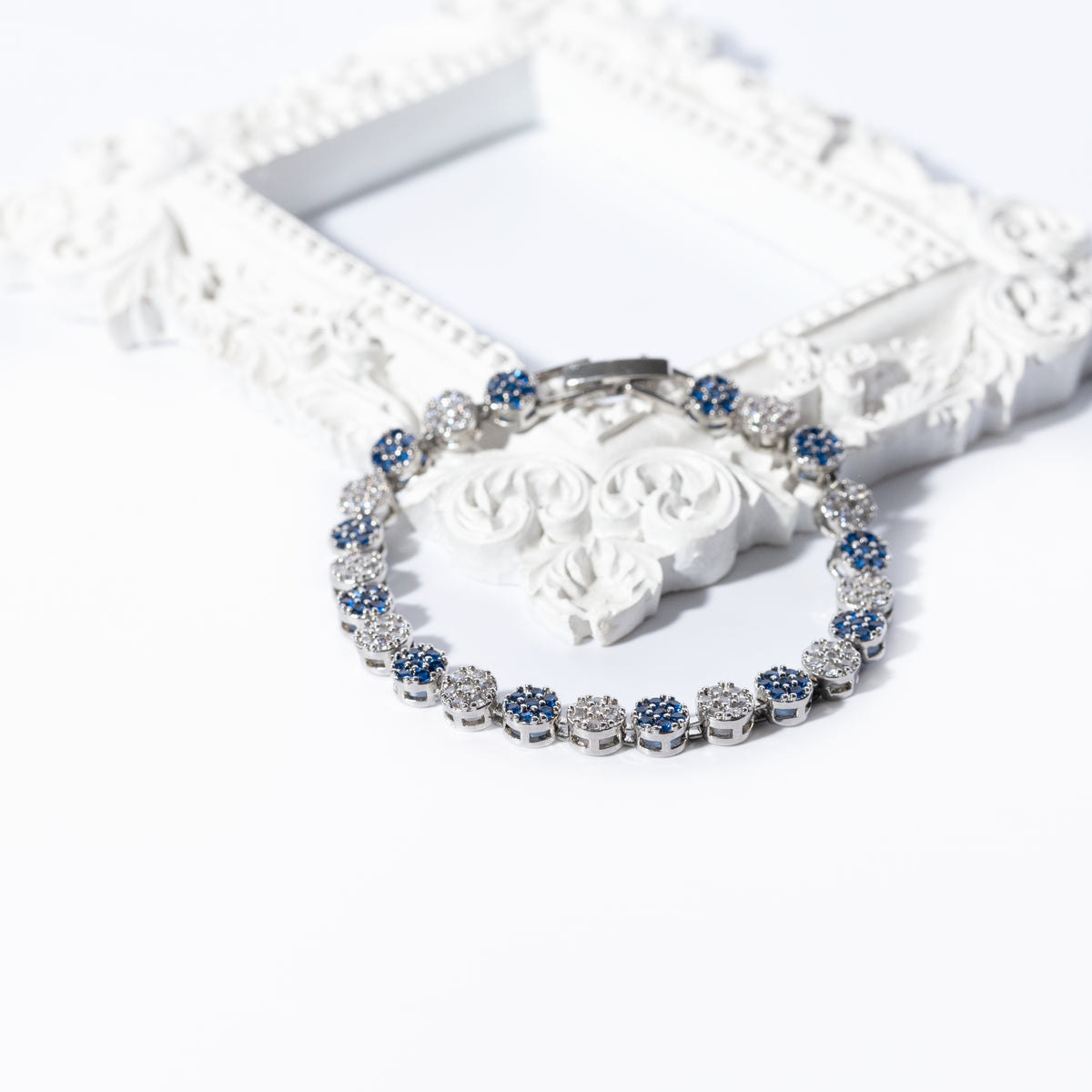 Silver-tone bracelet with alternating blue and clear round links beside an ornate white frame