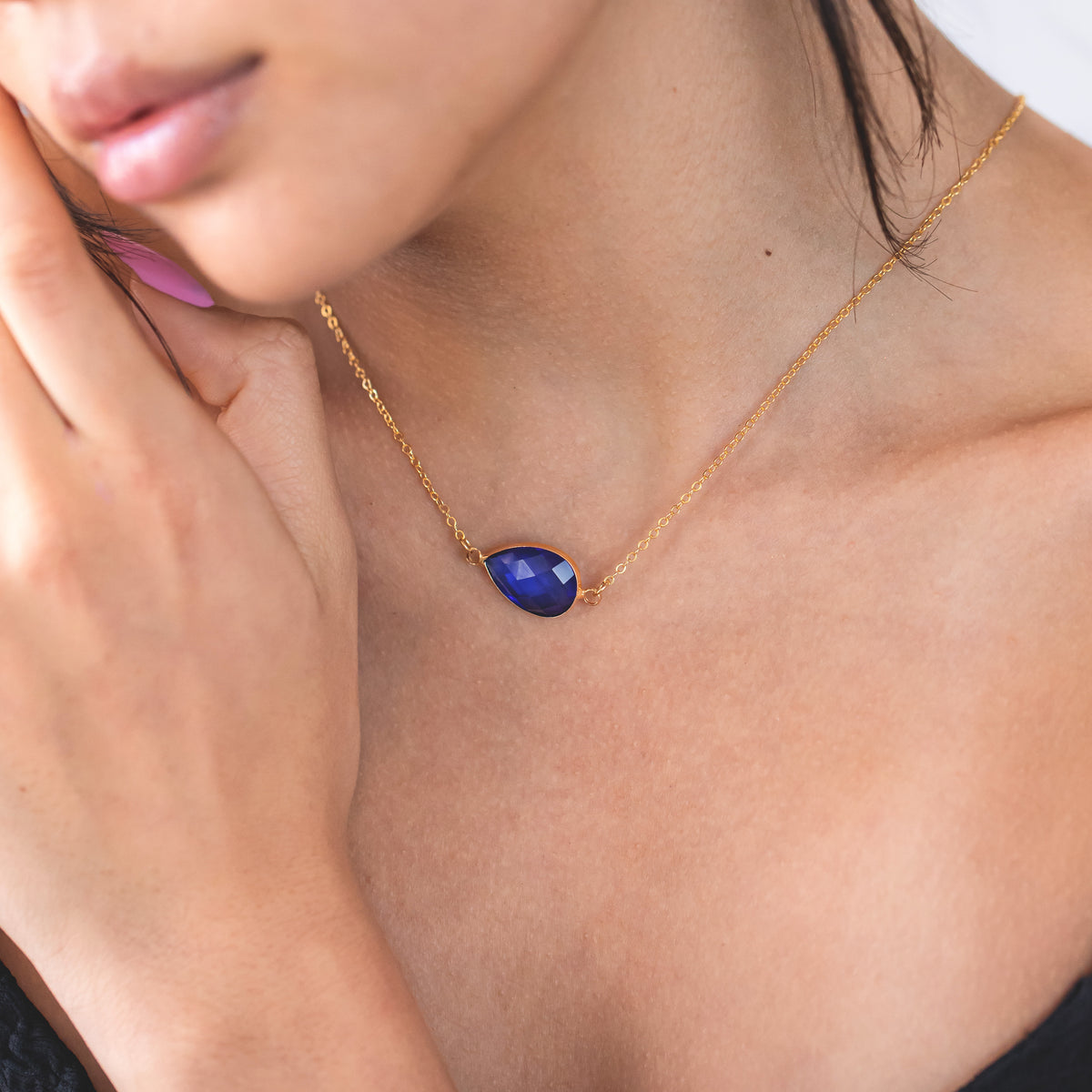 Gold-tone necklace with a dark blue faceted pendant worn at the neckline