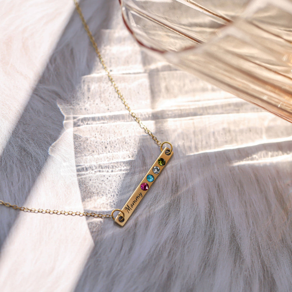 Gold-tone bar necklace engraved Mommy with four colored stones displayed on white fabric