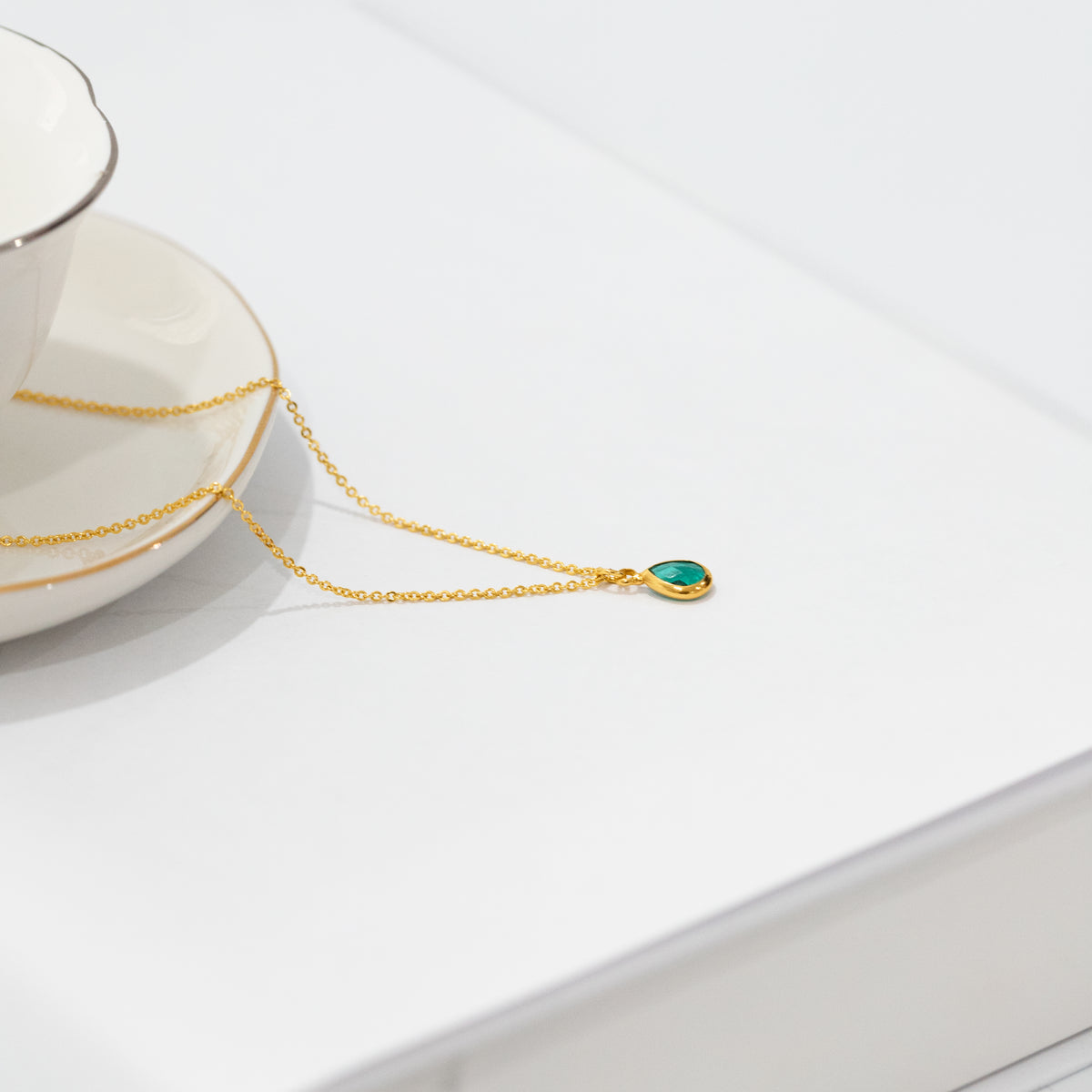 Gold-tone necklace with a green teardrop pendant displayed on a white surface