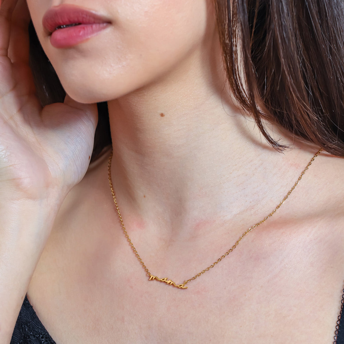 Gold-tone mama script necklace worn at the collarbone in a close-up view
