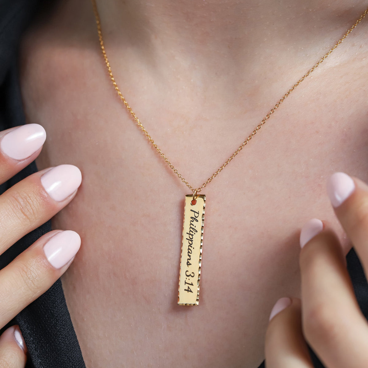 Gold-tone vertical bar necklace engraved with Philippians 3:14, worn on the neck with textured edges
