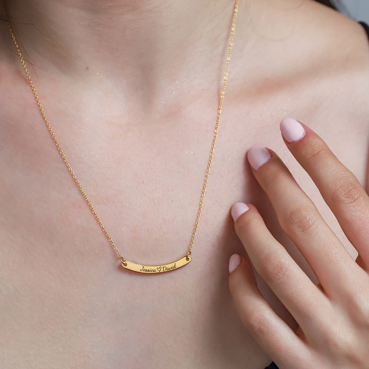 Gold-tone curved bar necklace with small engraved lettering worn at the neckline
