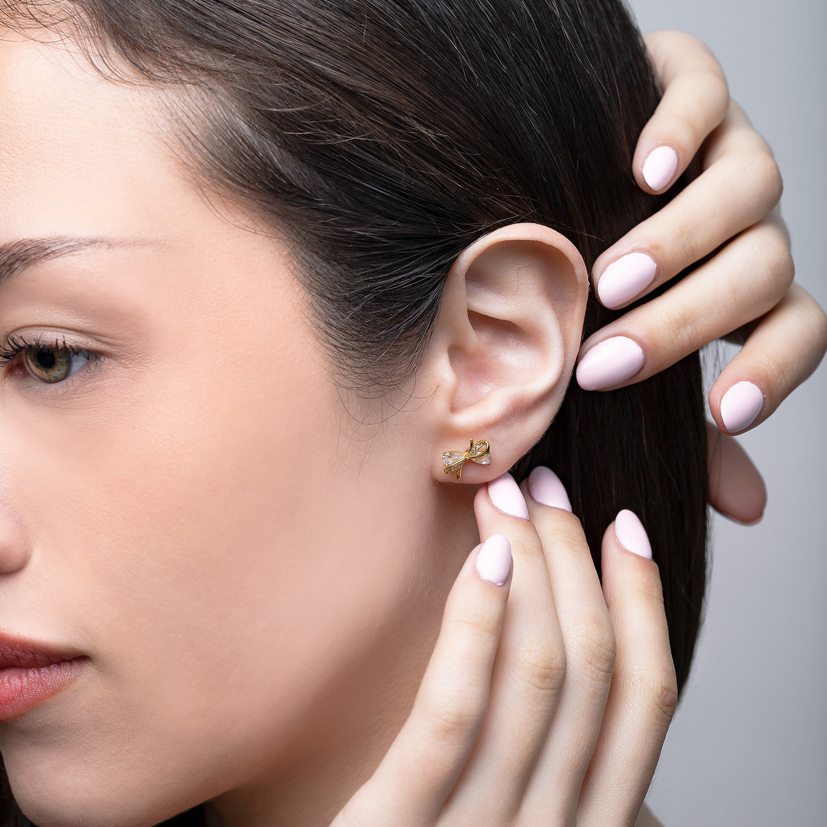 Close-up of a woman wearing gold earrings with a neutral background