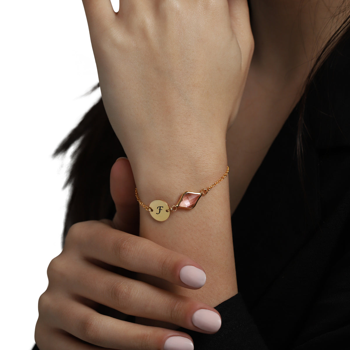 Gold-tone bracelet with engraved F initial disc and pink faceted stone worn on a wrist