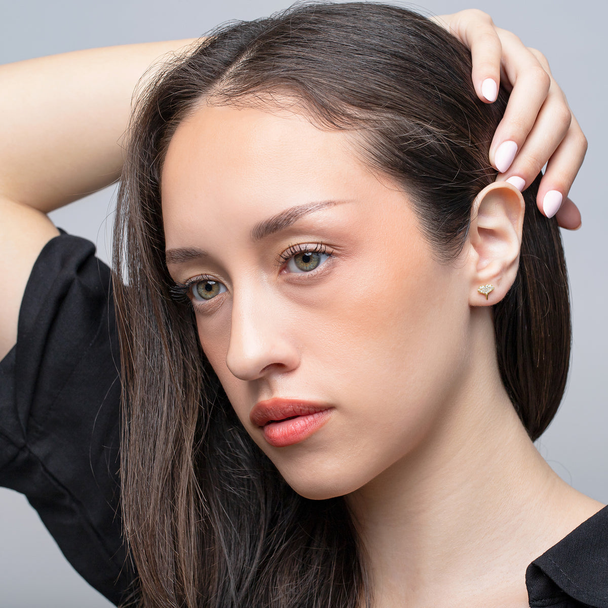 Gold-tone crystal-set whale tail stud earring worn by a model in a close-up portrait