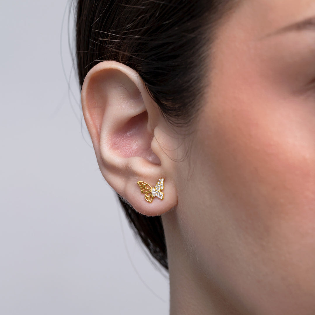 Gold butterfly earrings worn by a person on a plain background