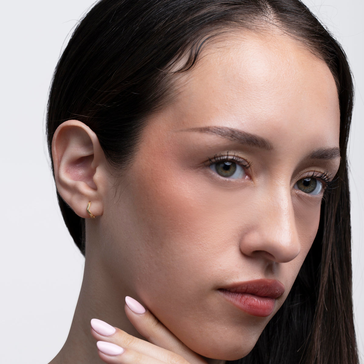 Gold-tone dainty huggie hoop earring worn on the ear in a front-facing portrait