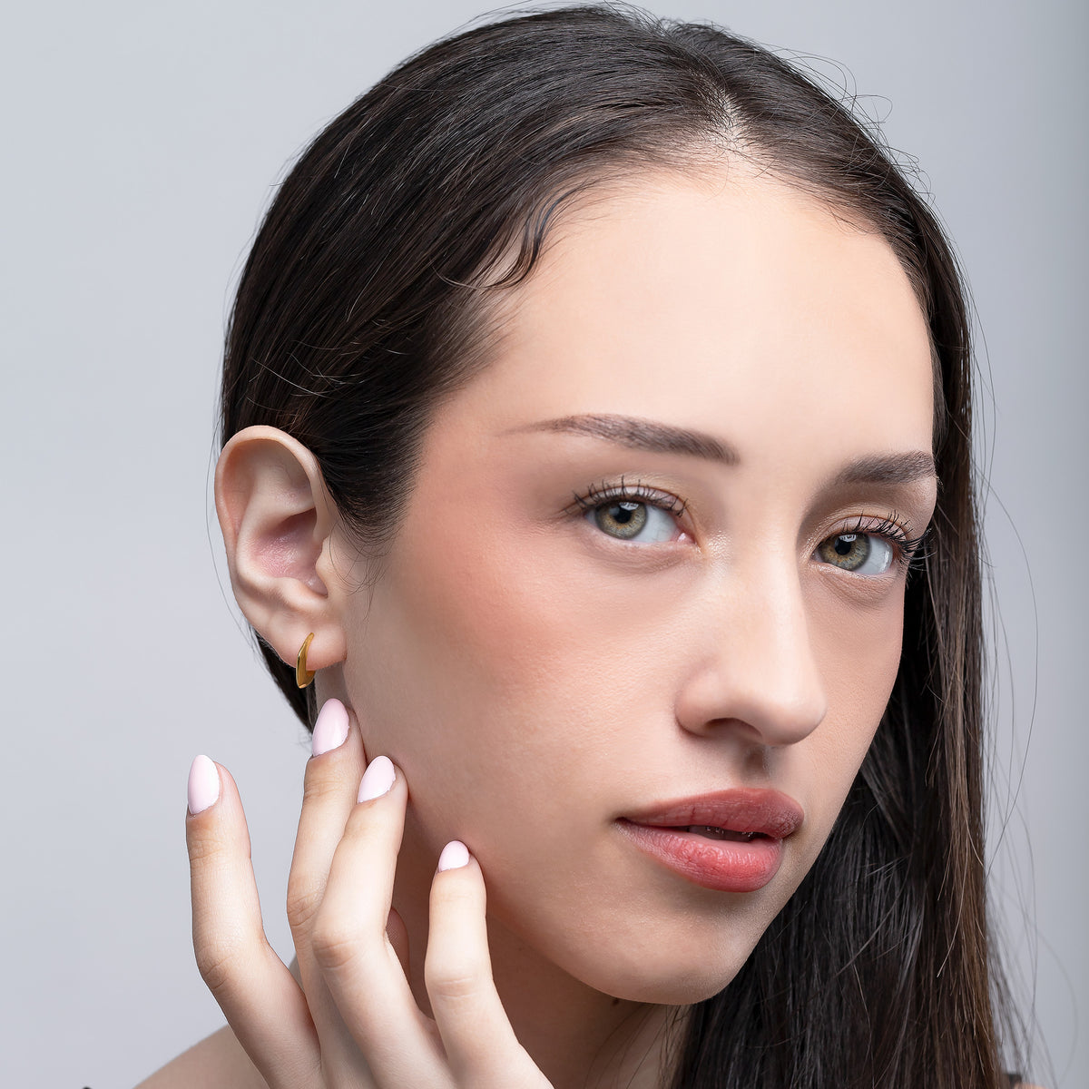 Gold-tone minimalist hook earring worn on the ear in a front-facing portrait