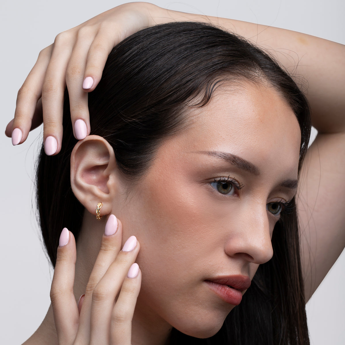 Gold-tone huggie hoop earring worn on a woman’s ear against a light gray background