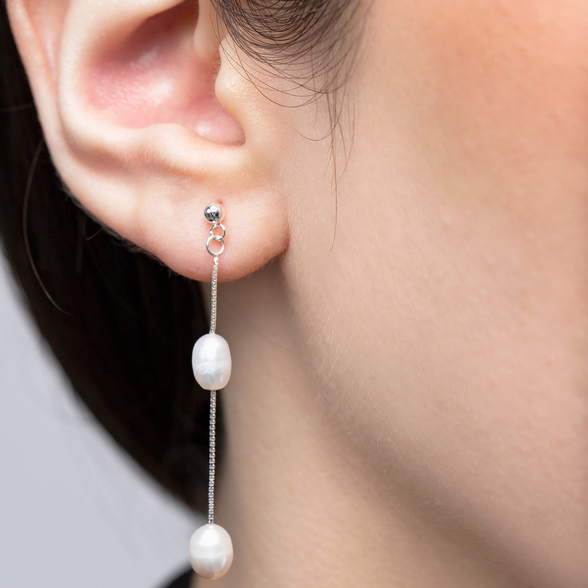 Silver-tone drop earring with two white pearl beads on a fine chain, worn on an ear
