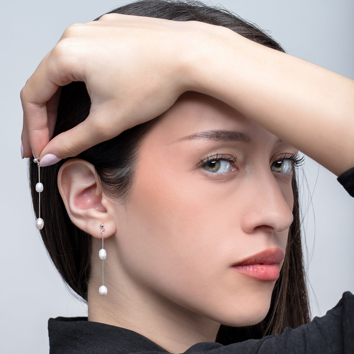 Silver-tone drop earrings with white pearl beads worn by a model, with one earring held beside the ear
