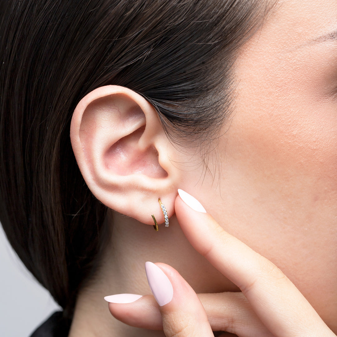 Close-up of an ear with a diamond earring, hand touching the earlobe.